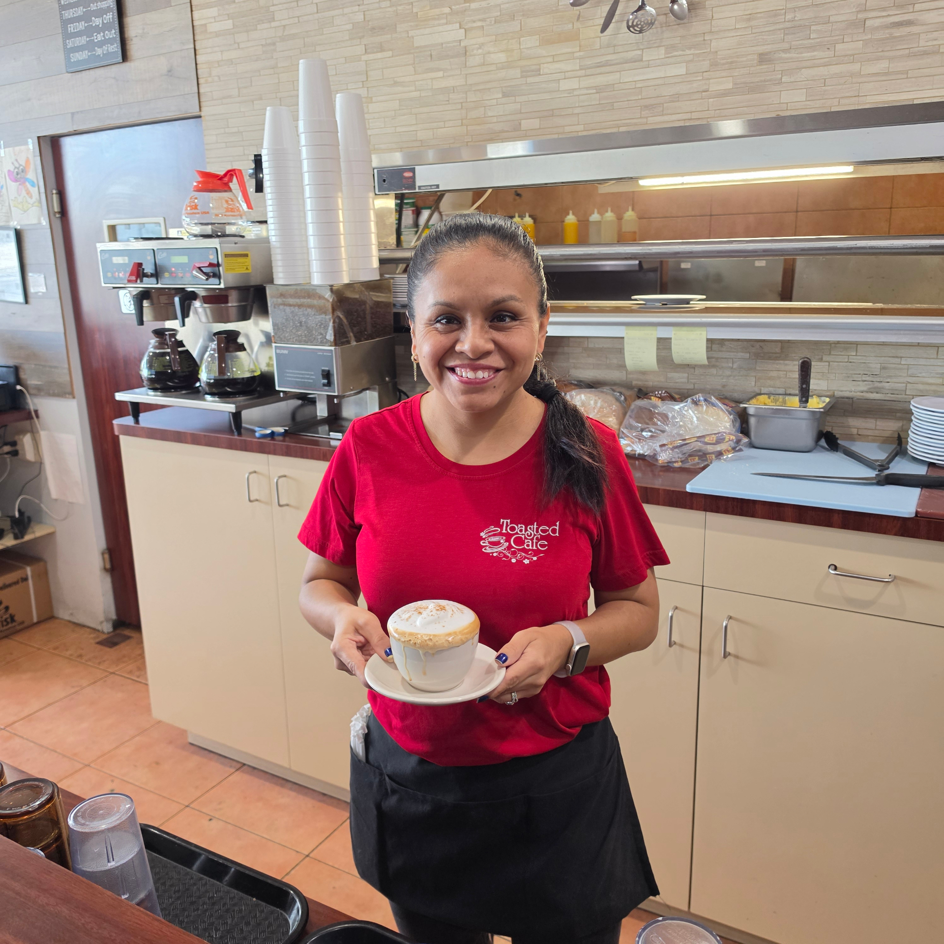 Smiling Toasted Cafe team member serving a fresh cappuccino